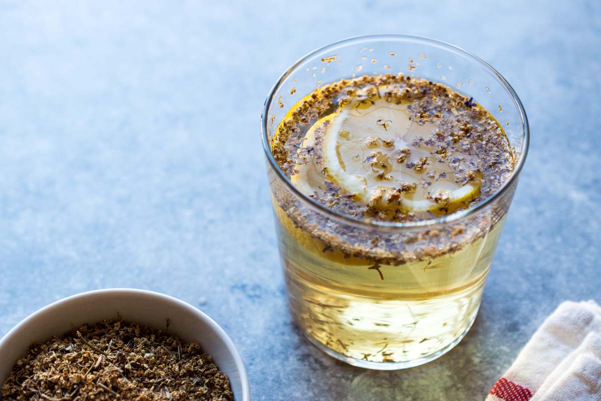 Un verre rempli de liquide et des fleurs de sureau séchées pour faire du sirop.