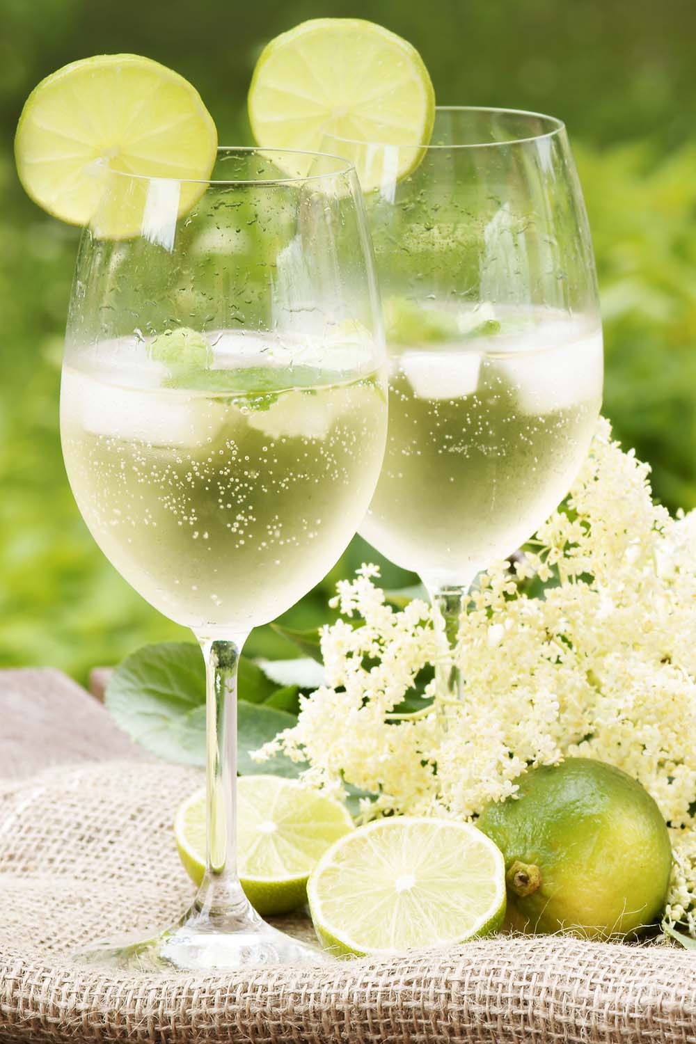 Deux cocktails de fleur de sureau dans des verres à vin avec des tranches de citron vert dans un jardin. Les fraîcheurs frais sont à droite.