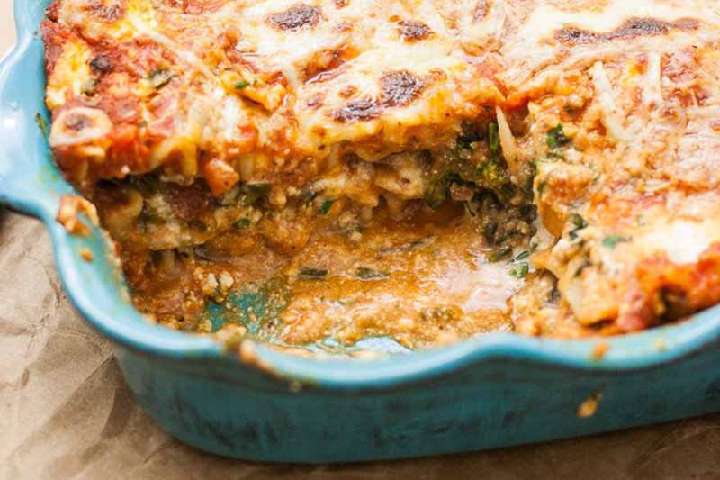 Un gros plan d'un bol en céramique bleu avec une lasagne sans viande fraîchement cuite. Une tranche en a été coupée révélant les couches de légumes riches en fromage.
