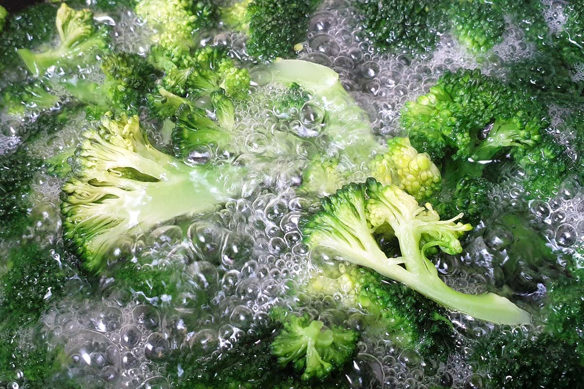 Un gros plan de fleurons de brocoli fraîchement récoltés dans de l'eau bouillante.
