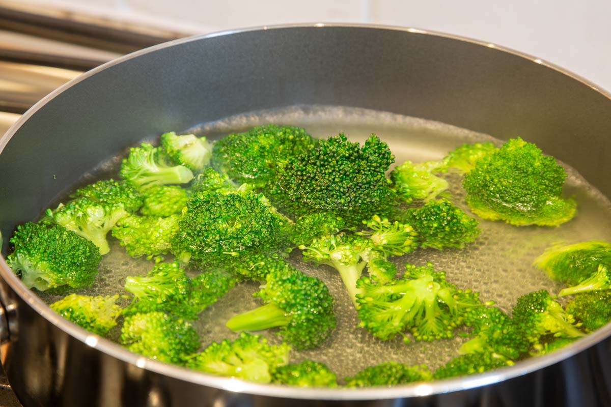 Un gros plan d'une casserole en métal avec de l'eau bouillante et des fleurons de brocoli vert vif.