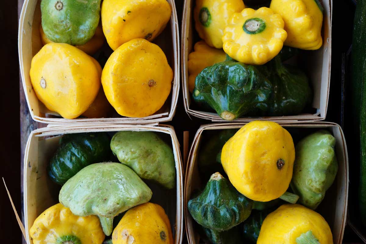 Une image en haut en haut de petites boîtes en bois contenant différentes variétés de poêle à galettes, ou courge de pétoncle, en différentes couleurs, jaune, vert foncé et clair.