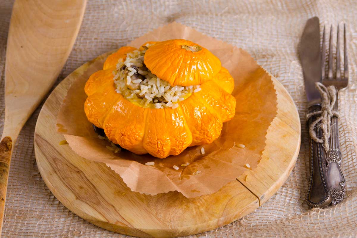 Un gros plan d'une courge Patty Patt en forme de pétoncle farcie de riz, placée sur une assiette en bois avec un couteau et une fourche à droite du cadre.
