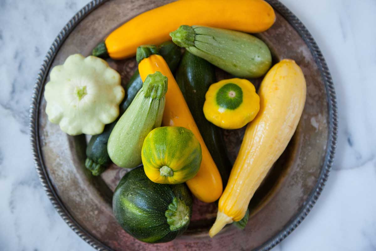 Une image en haut en haut en haut d'une plaque métallique avec un certain nombre de variétés de courges d'été différentes, en vert et jaune, réglées sur une surface en marbre.