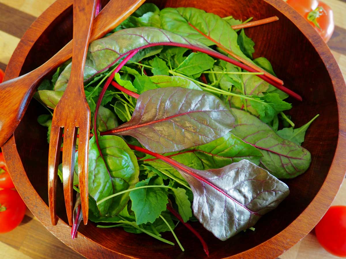 Une image horizontale rapprochée d'un salade en bois remplie de légumes verts mélangés.