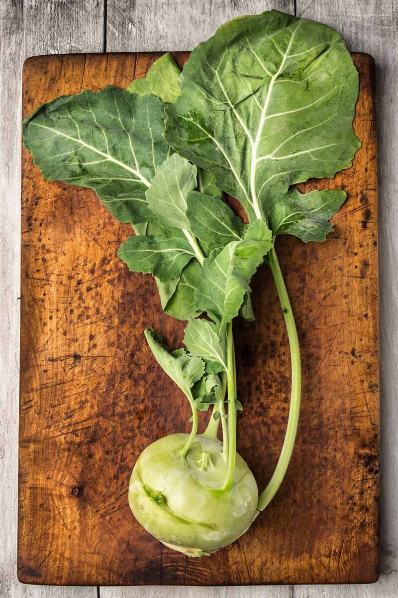 Une image verticale rapprochée d'un Kohlrabi fraîchement récolté avec des verts encore attachés sur une planche à couper le souffle en bois.