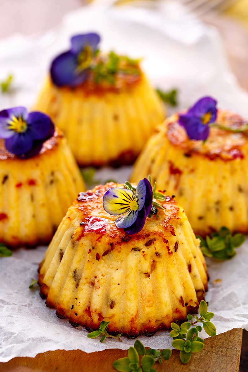 Une image verticale rapprochée de cupcakes frais du four décoré de pensées comestibles.