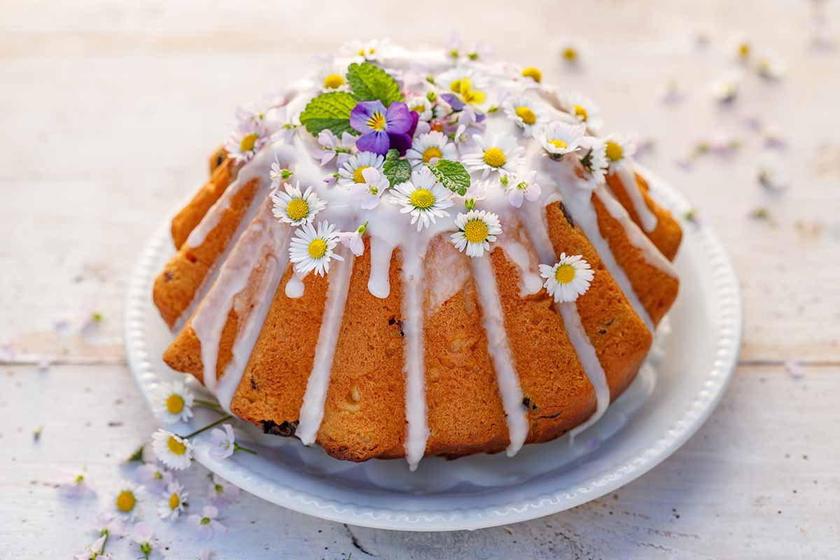 Une image horizontale rapprochée d'un gâteau de Pâques au glaçage blanc décoré de fleurs comestibles.