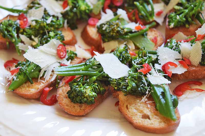 Une image horizontale en gros plan de tartines de rapini avec du parmesan râpé et des poivrons rouges hachés.