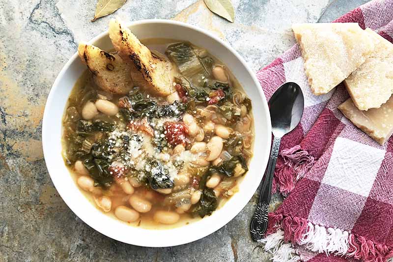 Une image horizontale en gros plan d'un bol de soupe aux haricots et aux légumes verts posé sur une surface en béton.