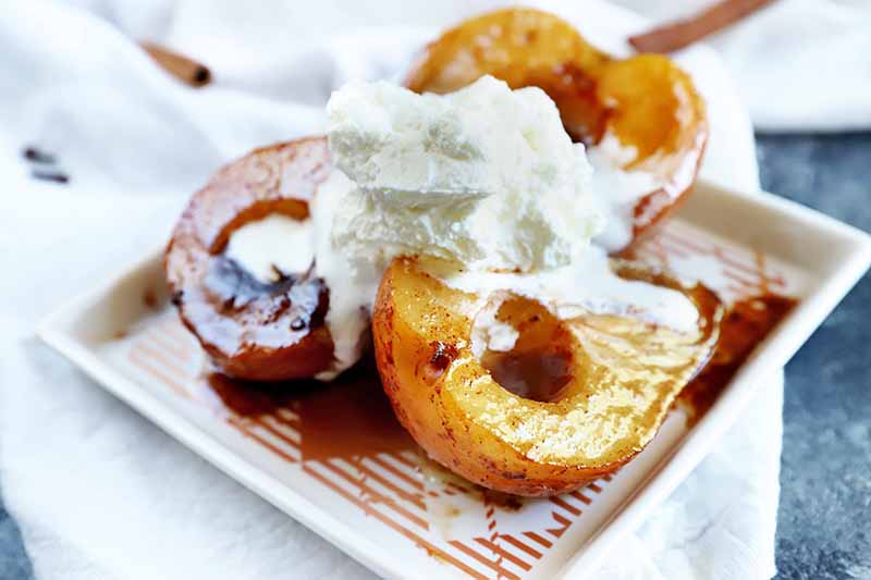 Une image horizontale en gros plan d'une assiette de poires caramélisées cuites au four garnies de crème fraîche et de sauce caramel.