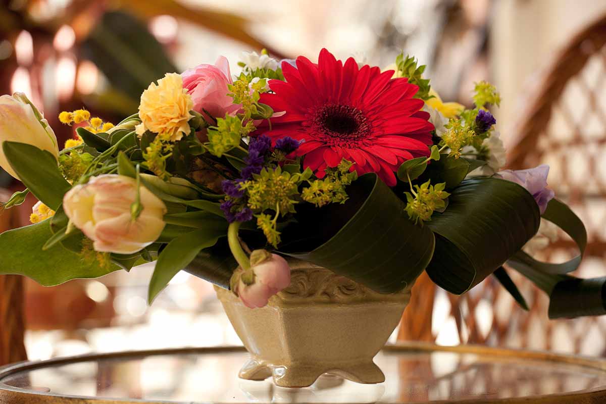 Image horizontale d'un bouquet de fleurs fraîches dans un petit récipient plat sur une table en verre.