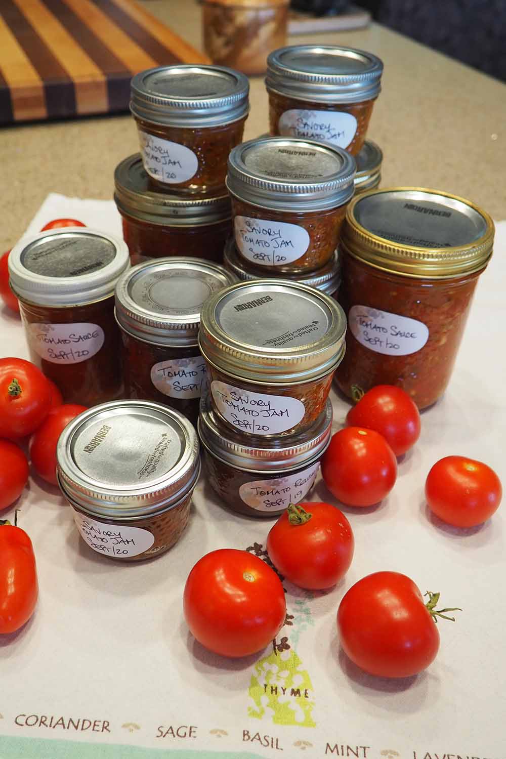 Une image verticale en gros plan d'une variété de sauces en conserve préparées à partir d'une récolte de tomates fraîches du jardin, avec des fruits mûrs éparpillés.